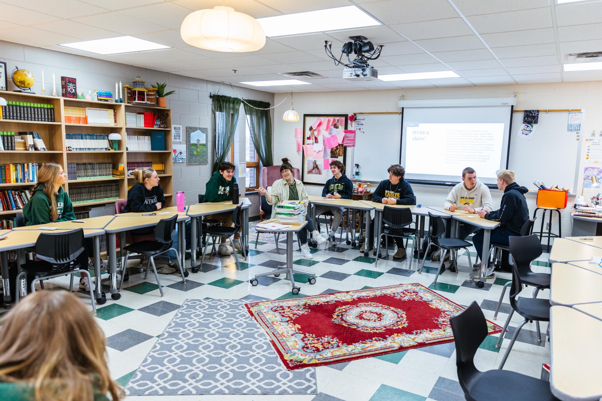 High school students seated in a semicircle in a New Life Academy classroom, participating in a lesson with desks arranged around the room.