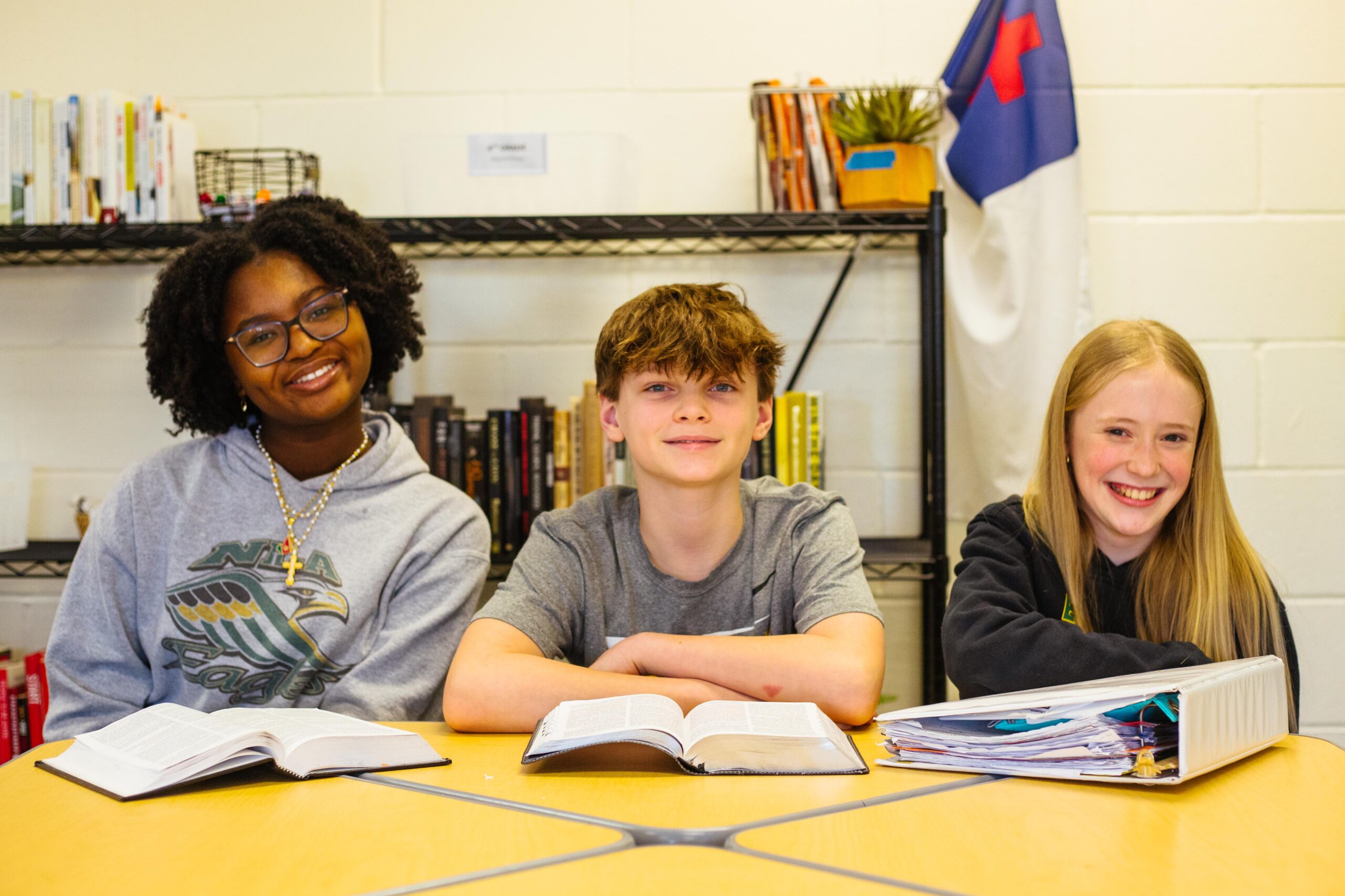 Three middle school students laughing in the hall with their backpacks on as they head to class.