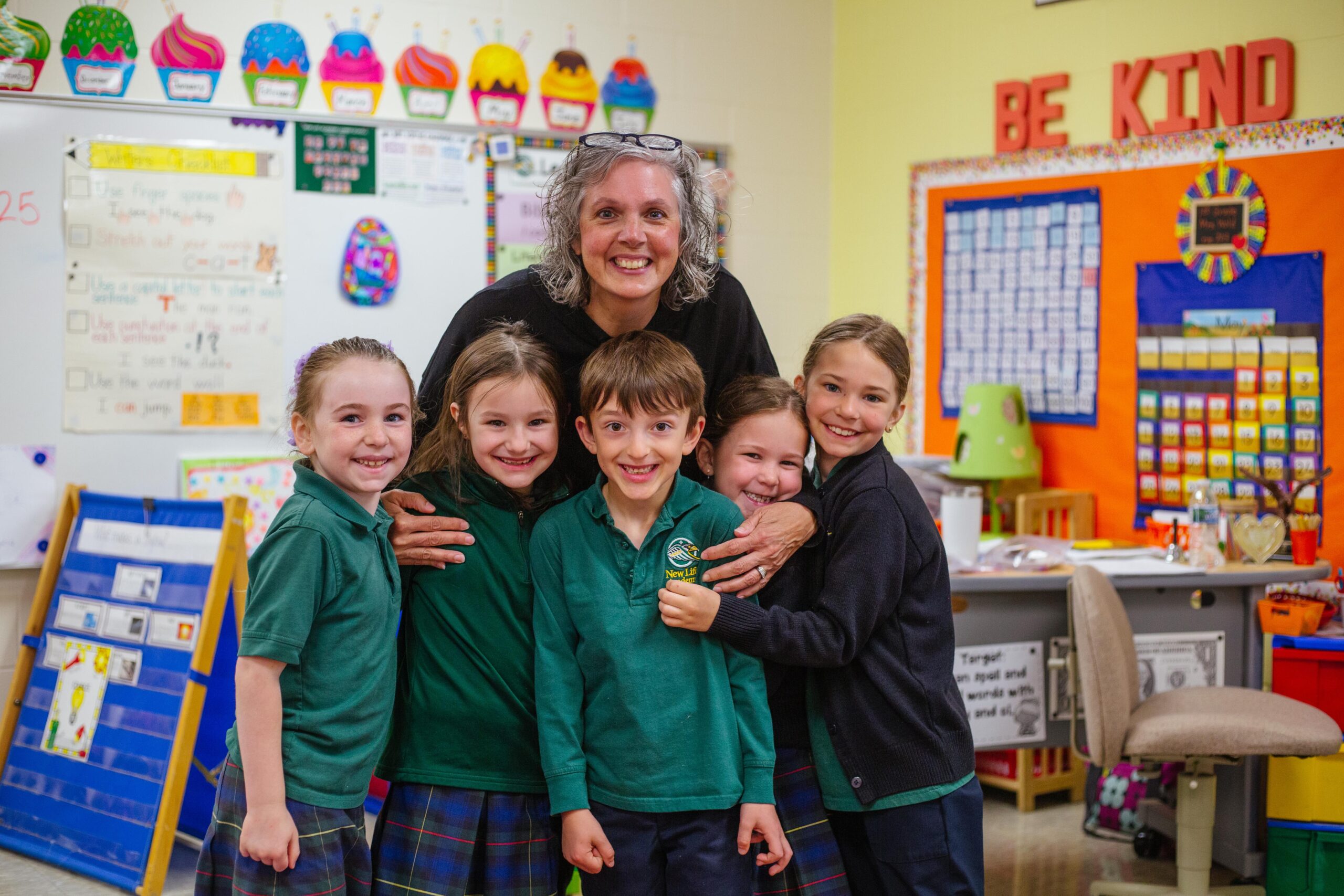 A teacher stands by students discussion a lesson with students seated at desks.