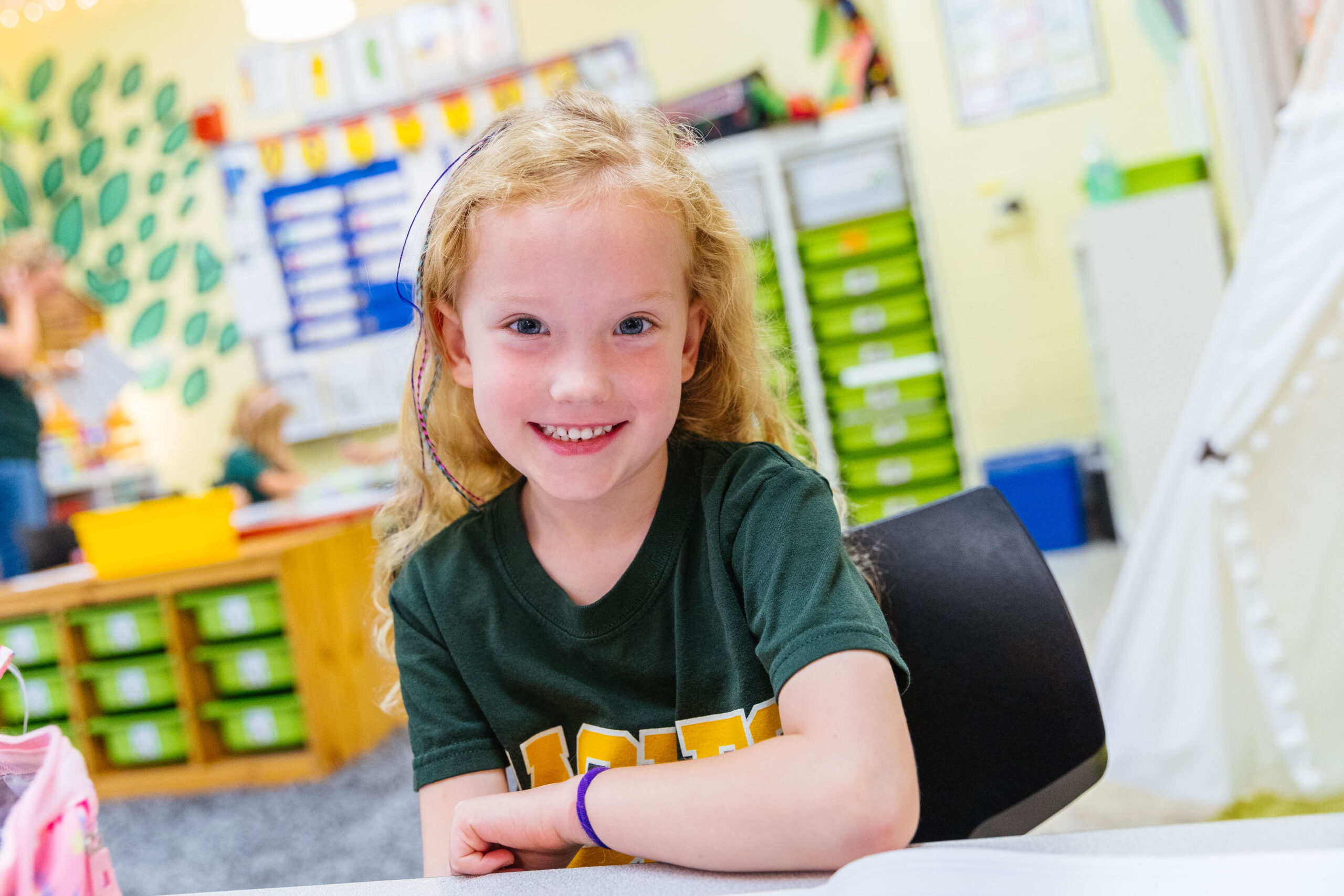 Kindergarten students sit around their classroom table learning from their teacher.
