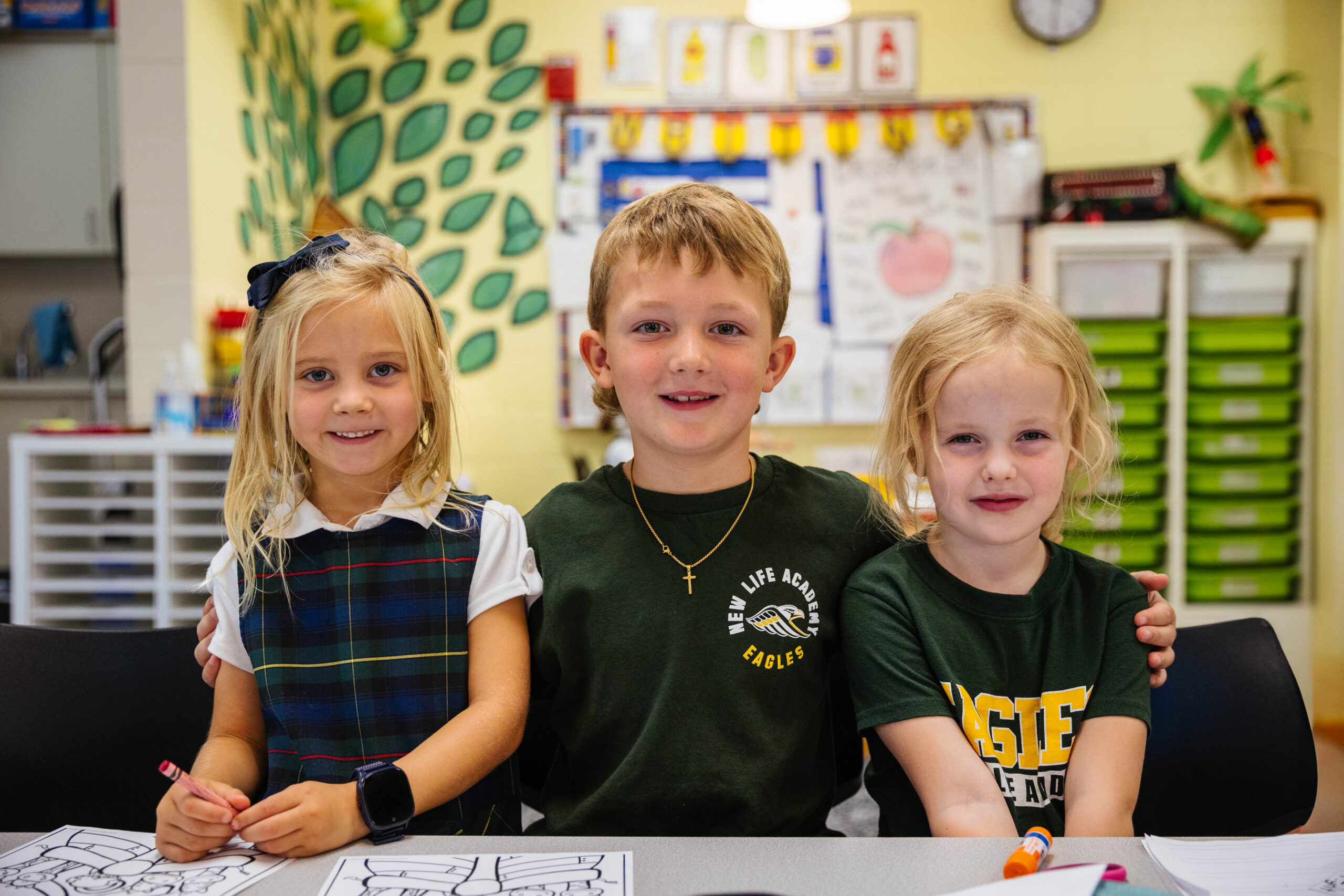 Kindergarten students sit around their classroom table learning from their teacher.