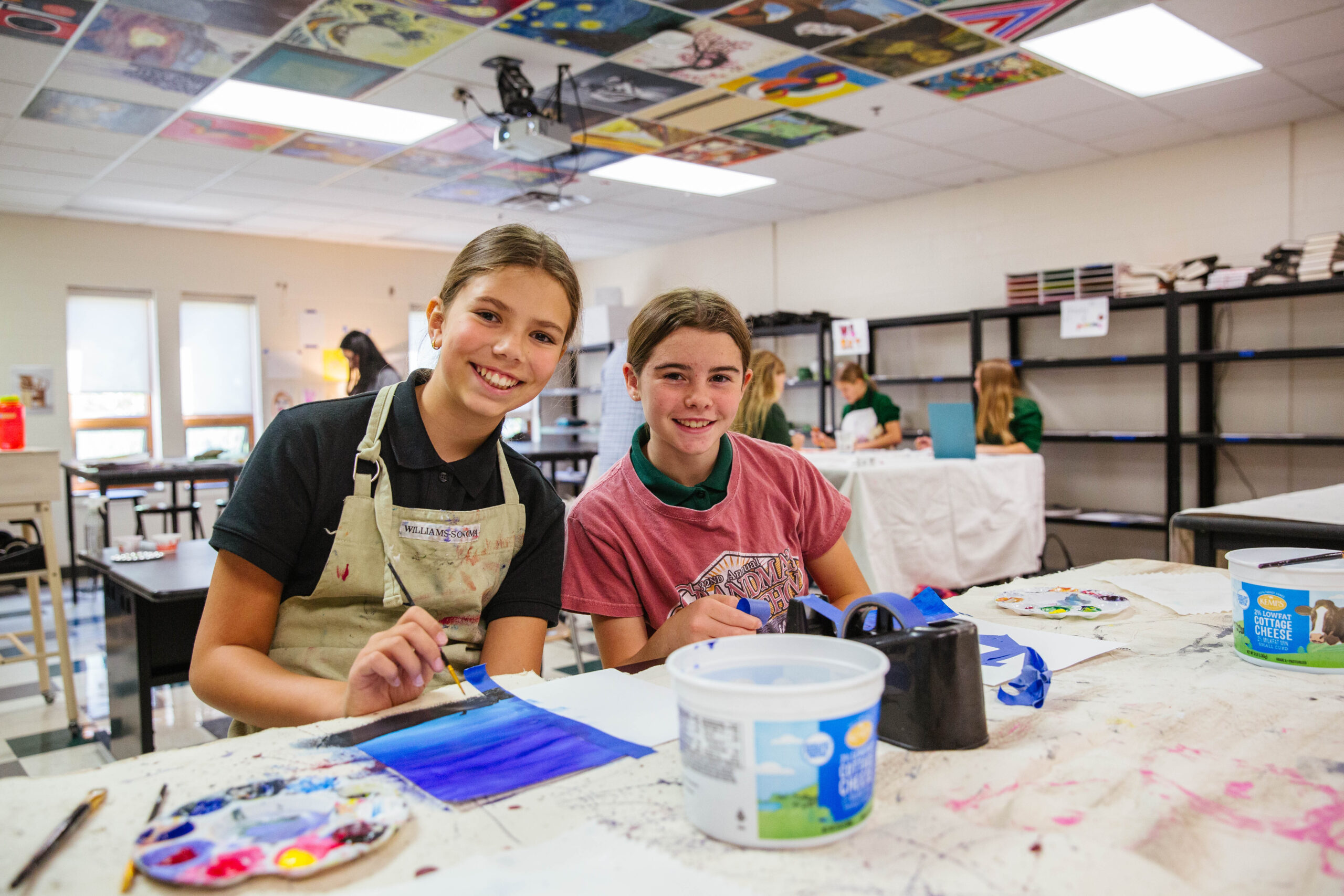 Middle School Bible teacher helps student on their computer during class as students in the background work on their assignments.