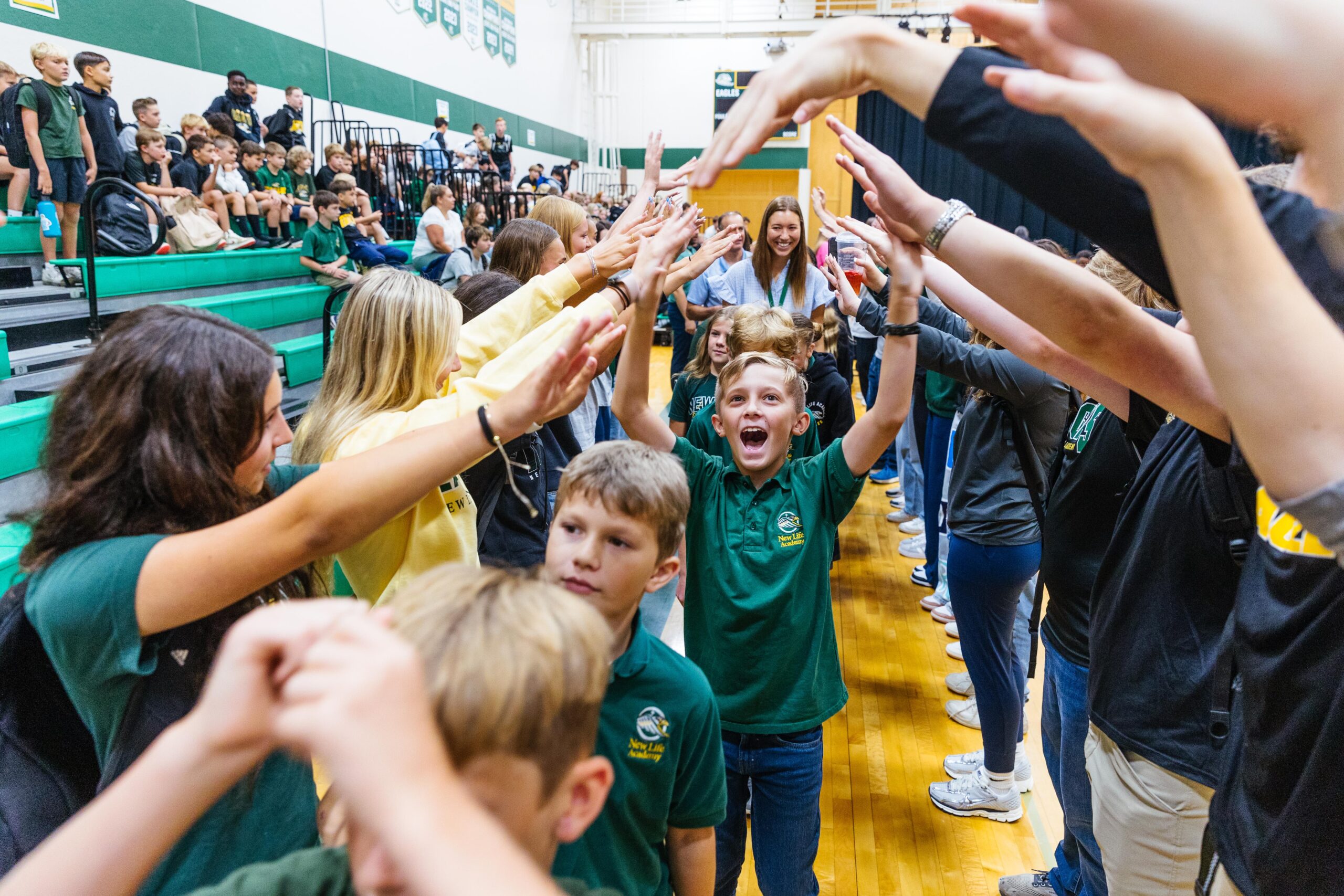 Students at New Life Academy cheerfully walking through a tunnel of raised arms during a school spirit event in the gym.