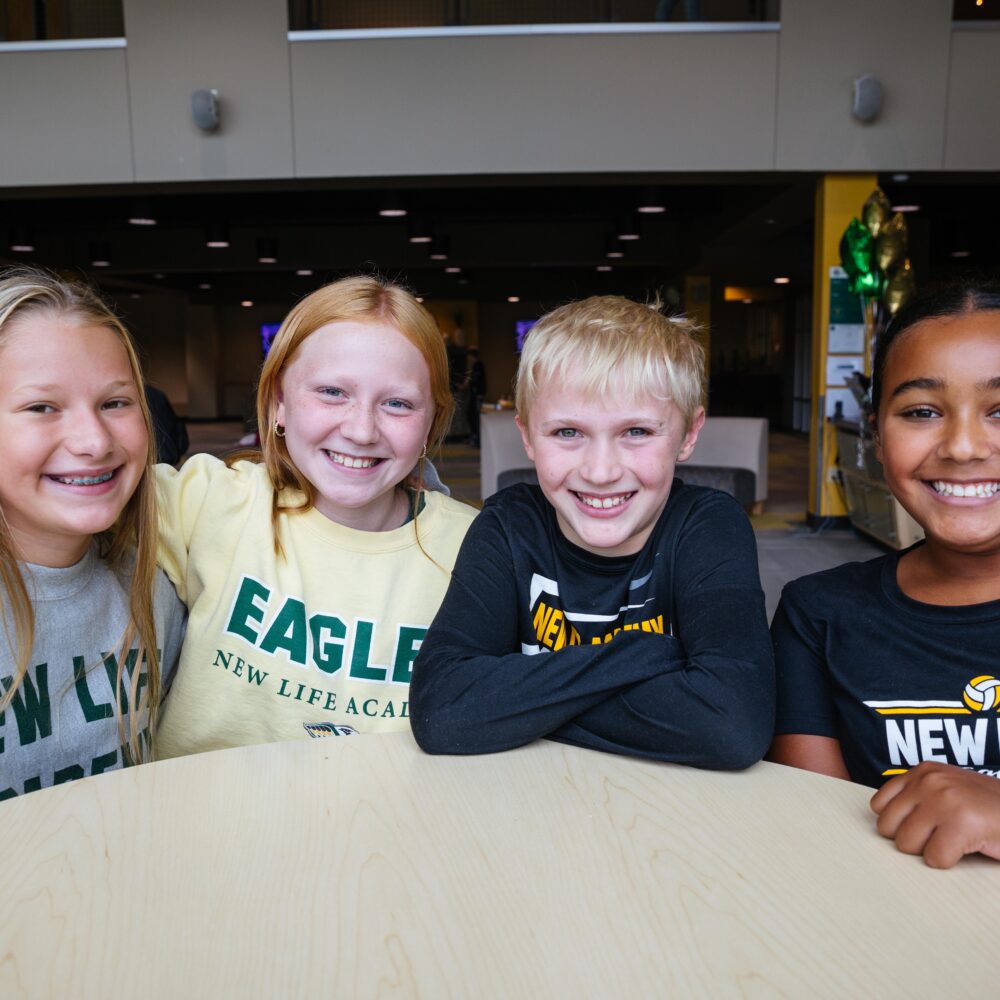 Four smiling middle school students at New Life Academy sitting together in the commons area.