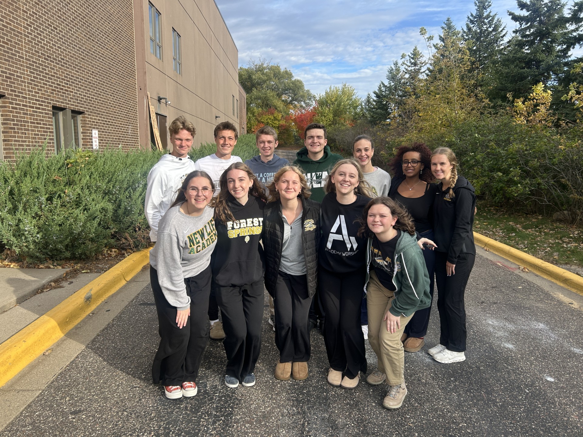Smiling female science teacher wearing an orange sweater stands in a colorful classroom with students working in the background
