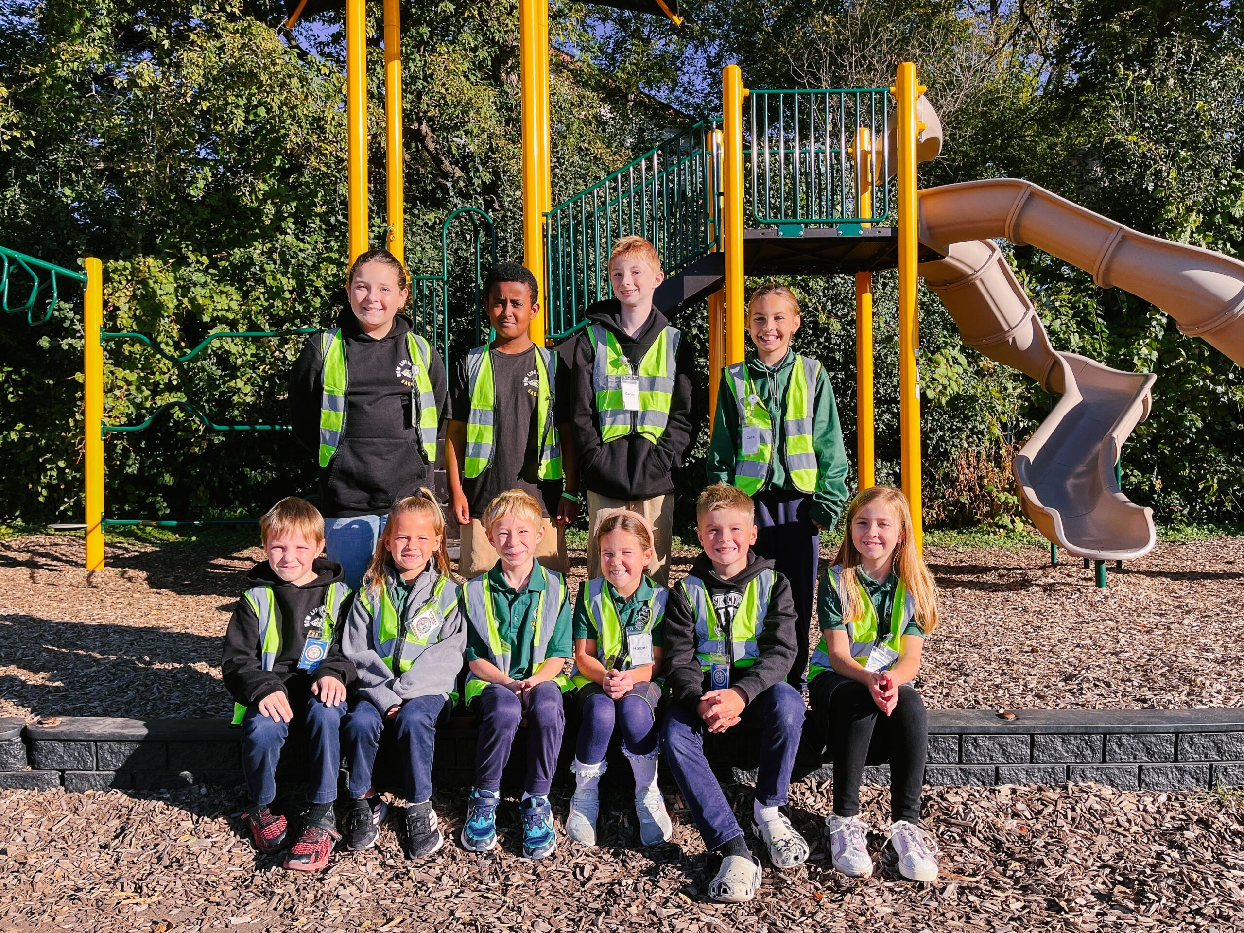 Smiling female science teacher wearing an orange sweater stands in a colorful classroom with students working in the background