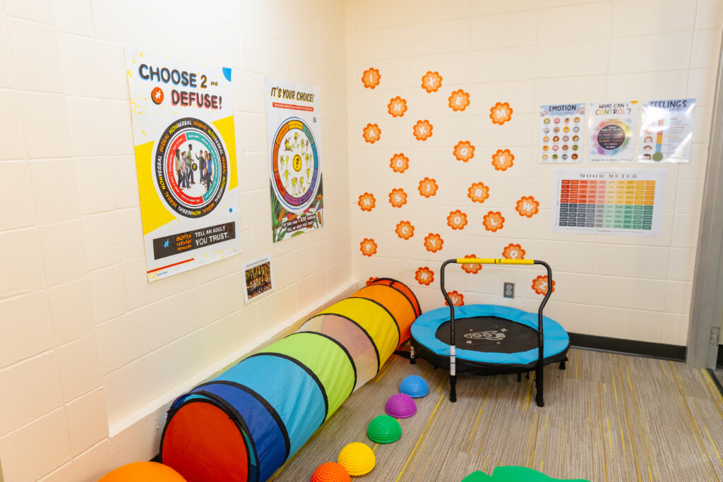 Colorful sensory playroom with posters on emotional regulation, a rainbow tunnel, balance pods, and a small trampoline