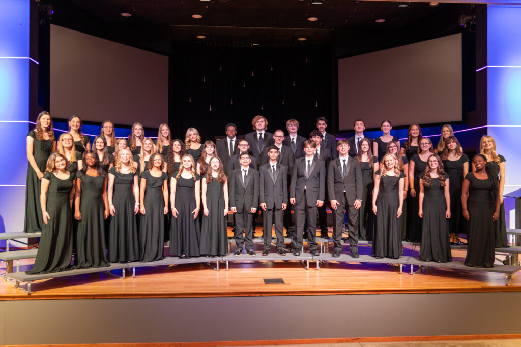 Upper School Concert Choir at New Life Academy posed on stage in formal black attire for a group photo.