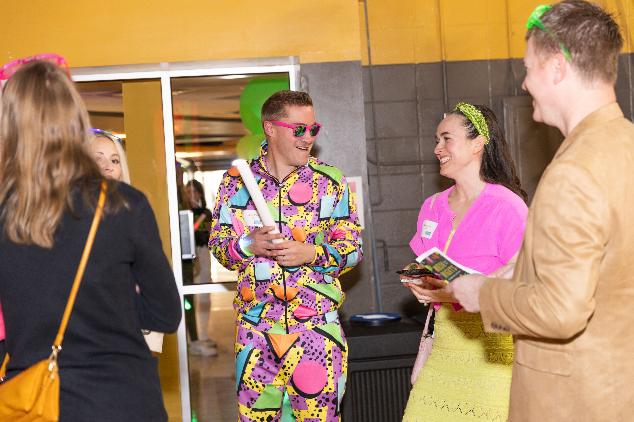 Guests dressed in vibrant neon-themed outfits chatting during New Life Academy’s Neon Nights Celebration Auction fundraising event.