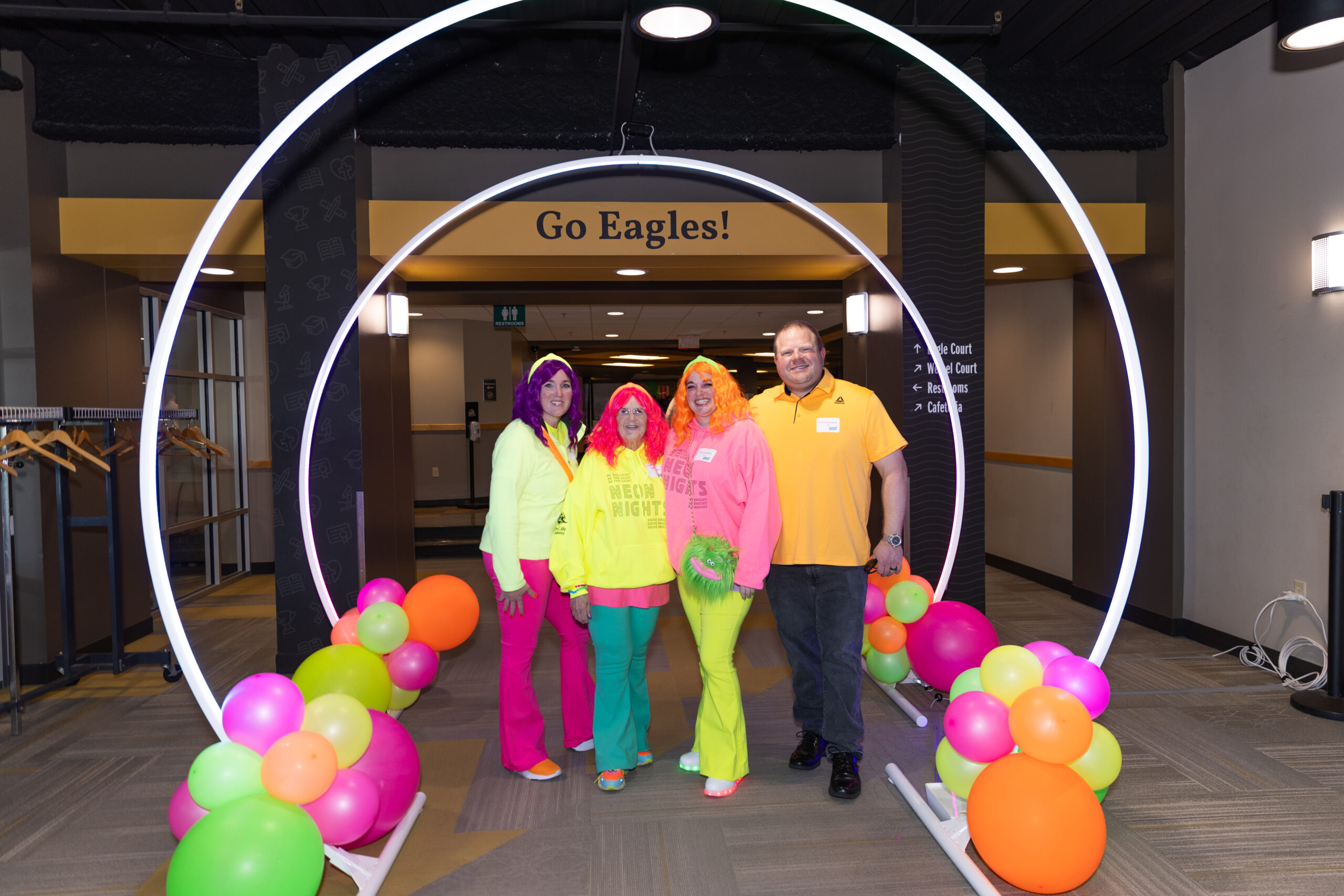 Guests in bright neon outfits posing under a glowing archway at New Life Academy’s Neon Nights Celebration Auction.