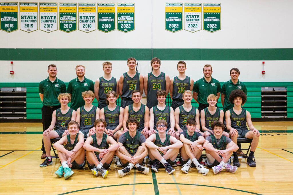 NLA Varsity Boys Basketball team group photo from the 2022–2023 season, taken in the gym with championship banners displayed overhead.