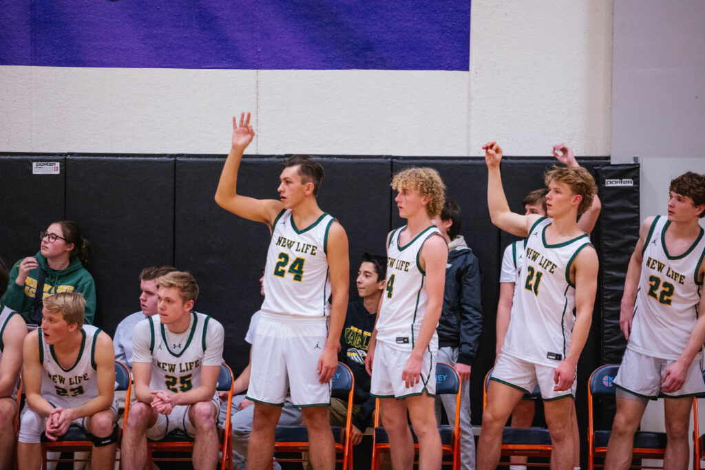NLA Varsity Boys Basketball players during 2022–2023 game play, featuring alumni Charles Bryant supporting his teammates.