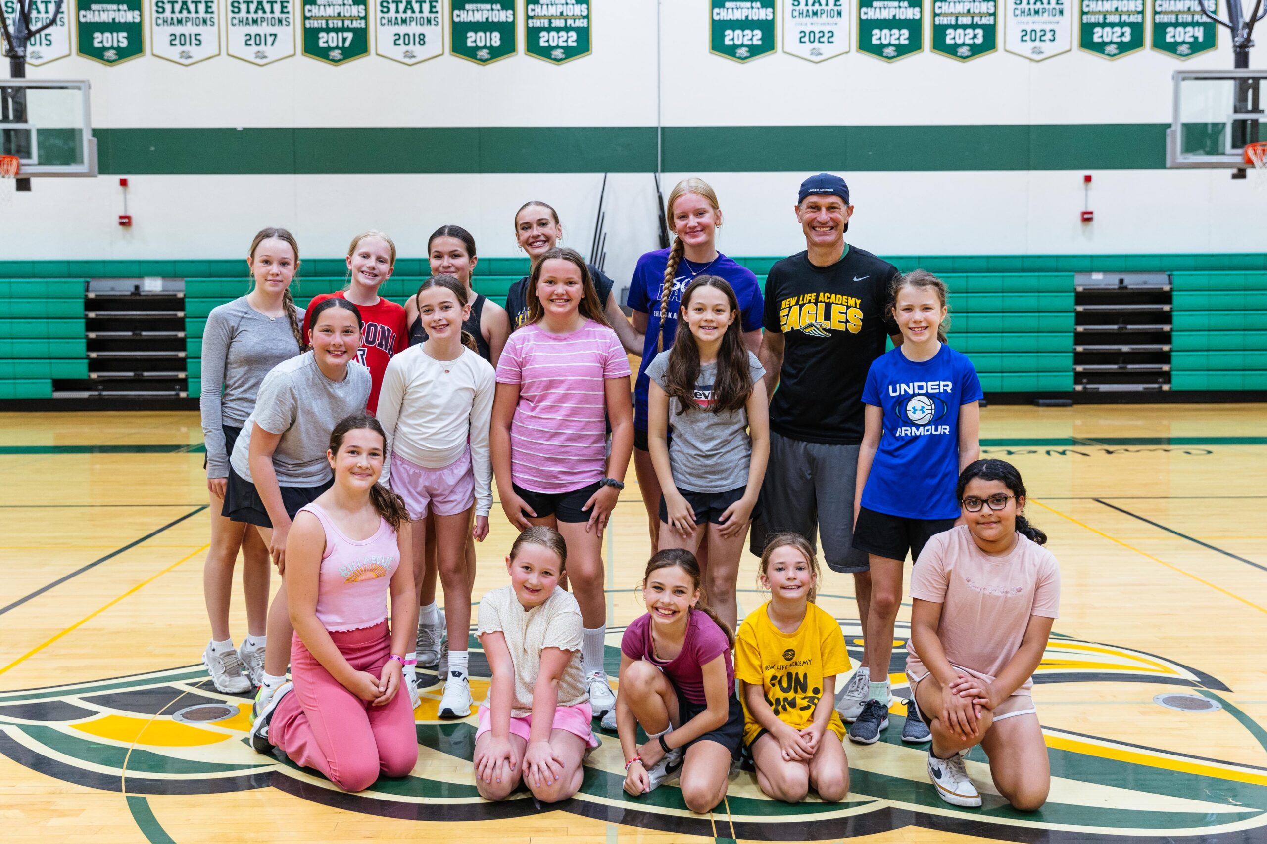 Group of students and a teacher posing together in the gym during a New Life Academy teacher led summer camp.