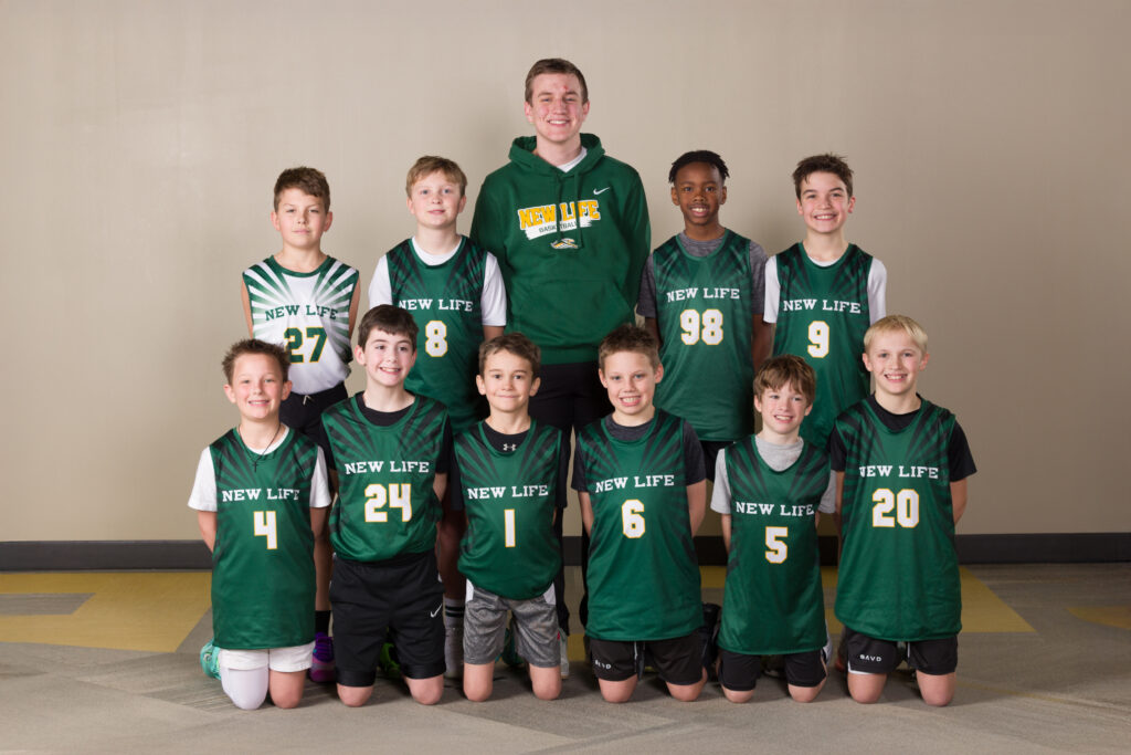 Middle school basketball team from New Life School posing together in green jerseys with coaches standing behind them."