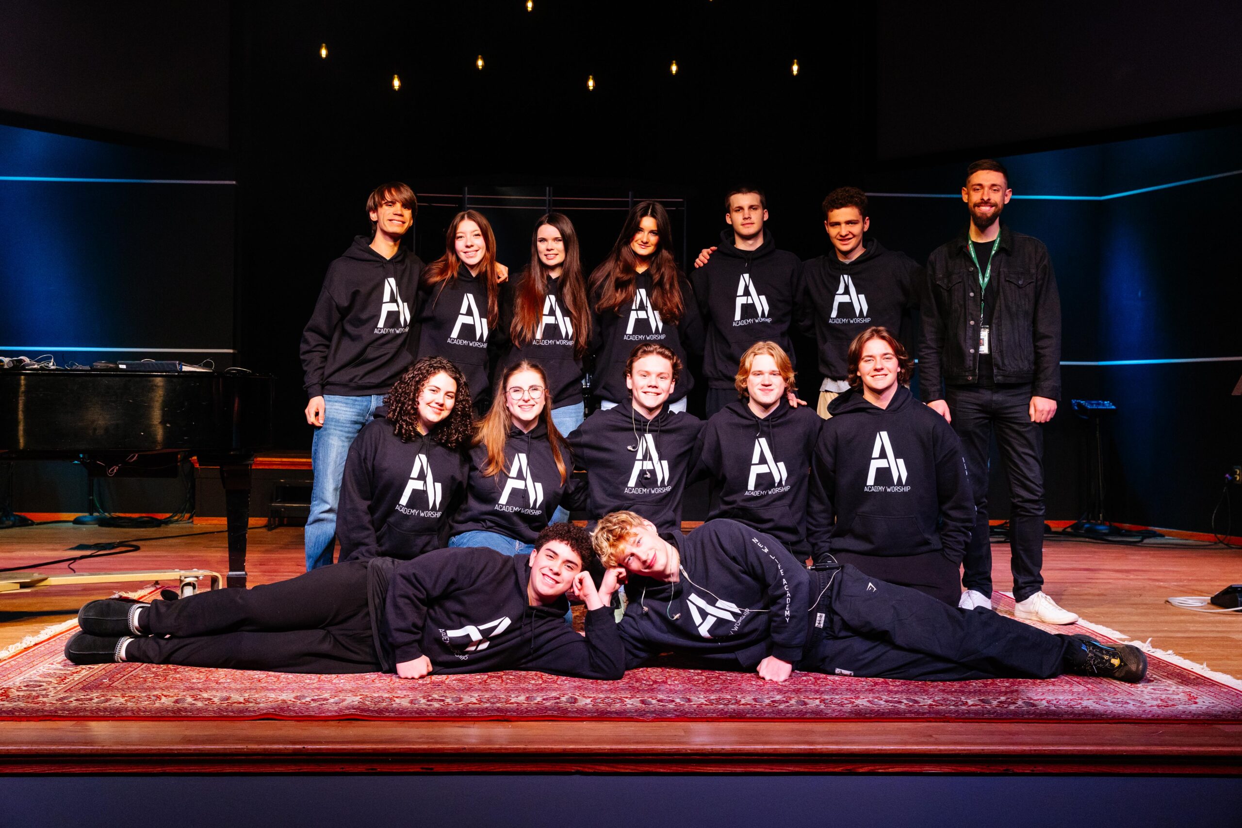 New Life Academy Worship class and student team posing together on stage in the chapel.