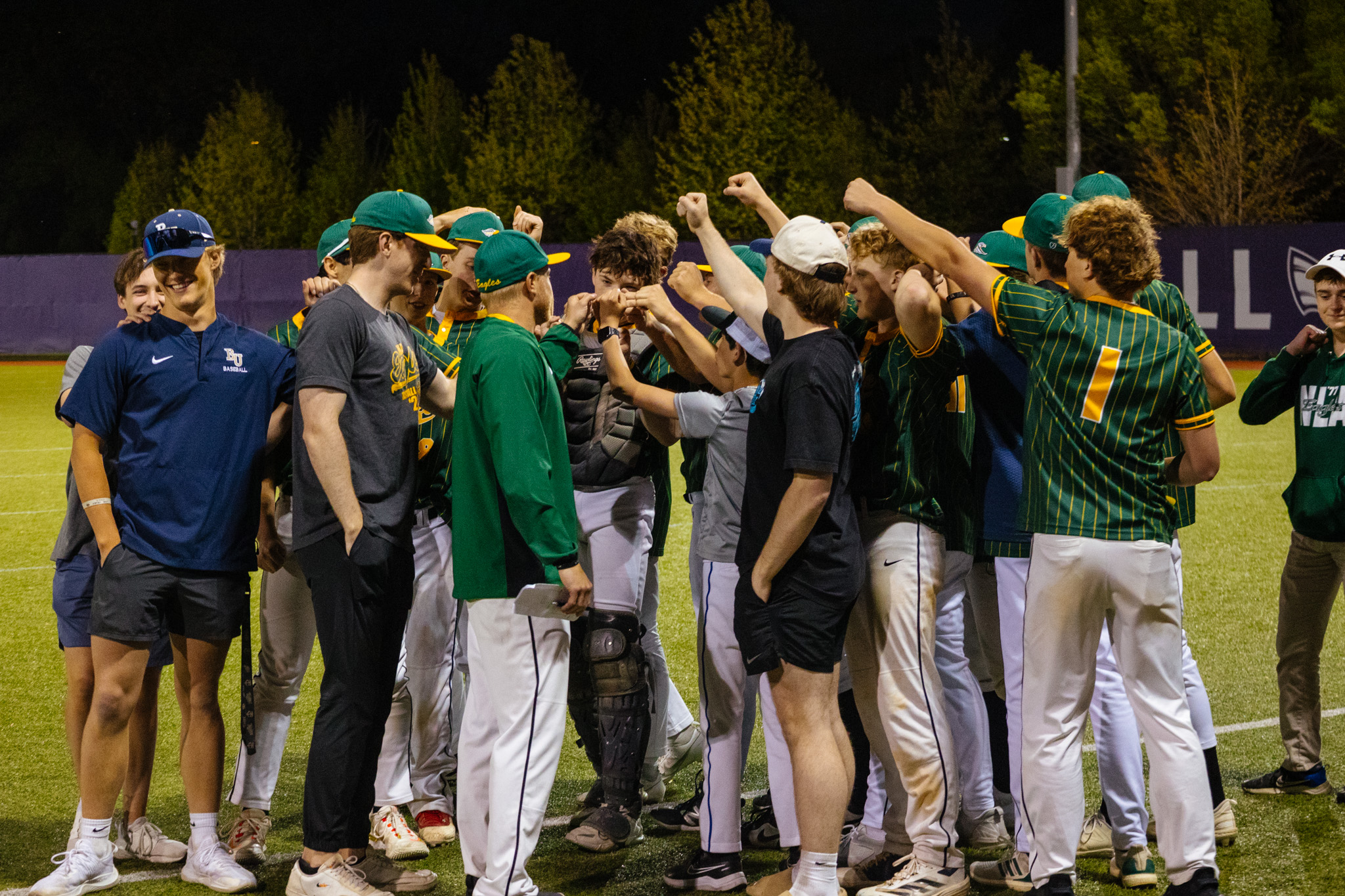 New Life Academy Boys Varsity Baseball Team huddled together on the field during a night game.