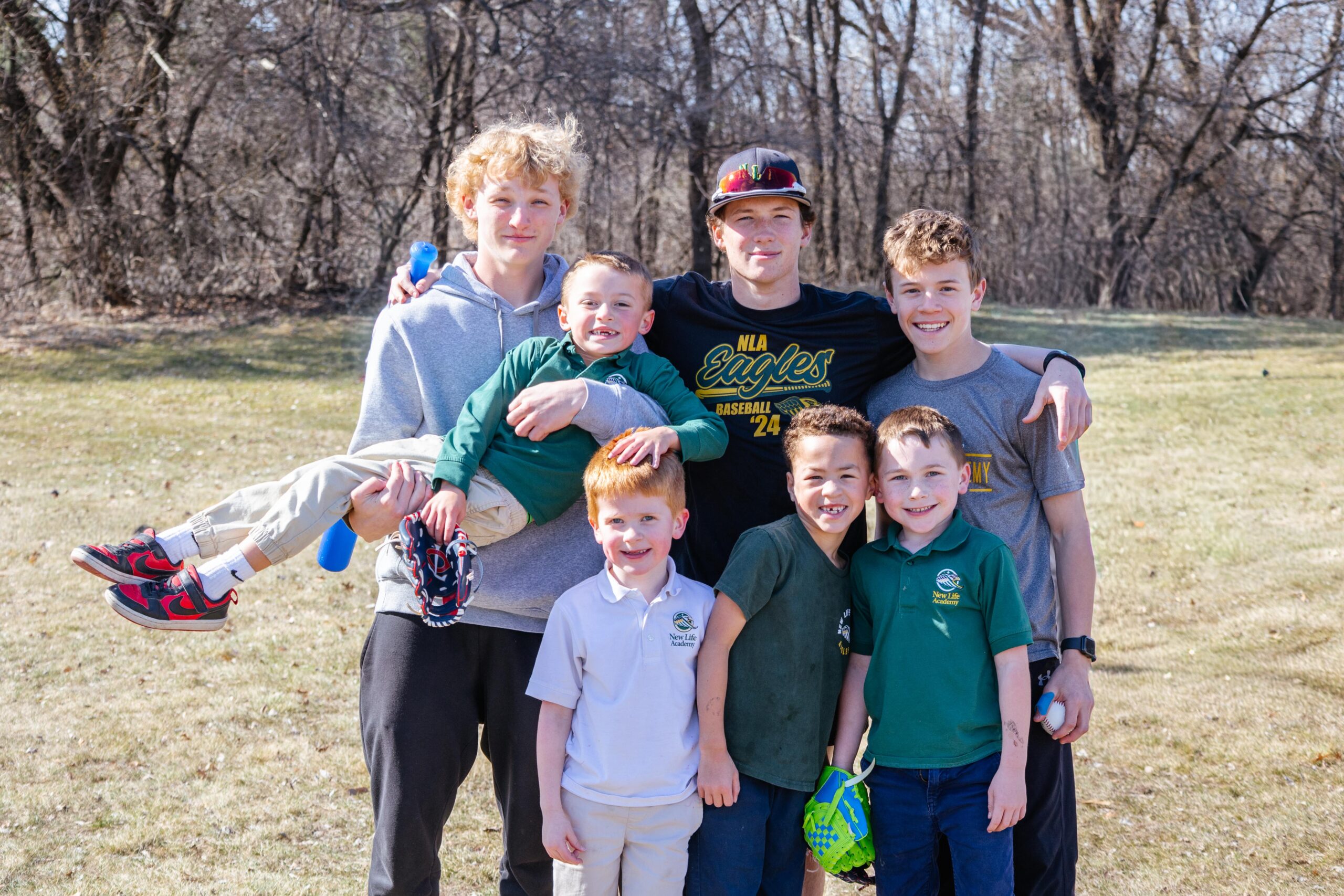 High school baseball players mentoring younger New Life Academy Junior Eagles athletes outdoors